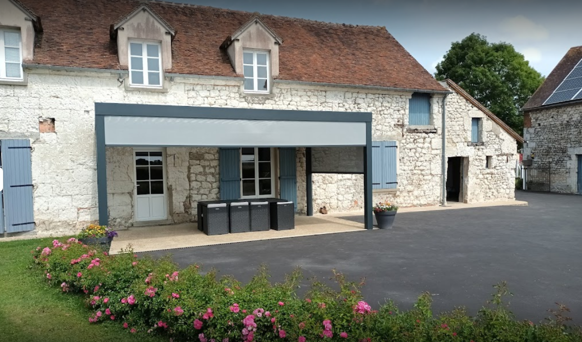 grande pergola bioclimatique pose sur la terrasse d'une grande maison en normandie avec des stories sur les côtés de la pergola pour protéger des intempéries