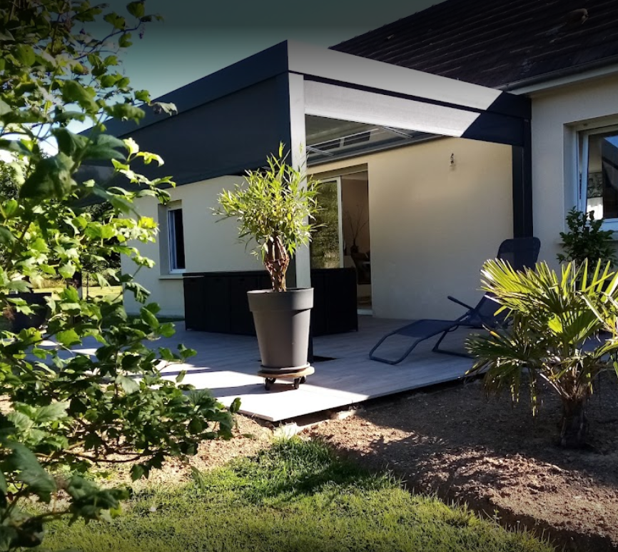 Pergola bioclimatique aux lames orientables posée sur la terrasse d'une maison en Normandie avec des stores sur chaque côté de la pergola pour protéger du vent et de la pluie